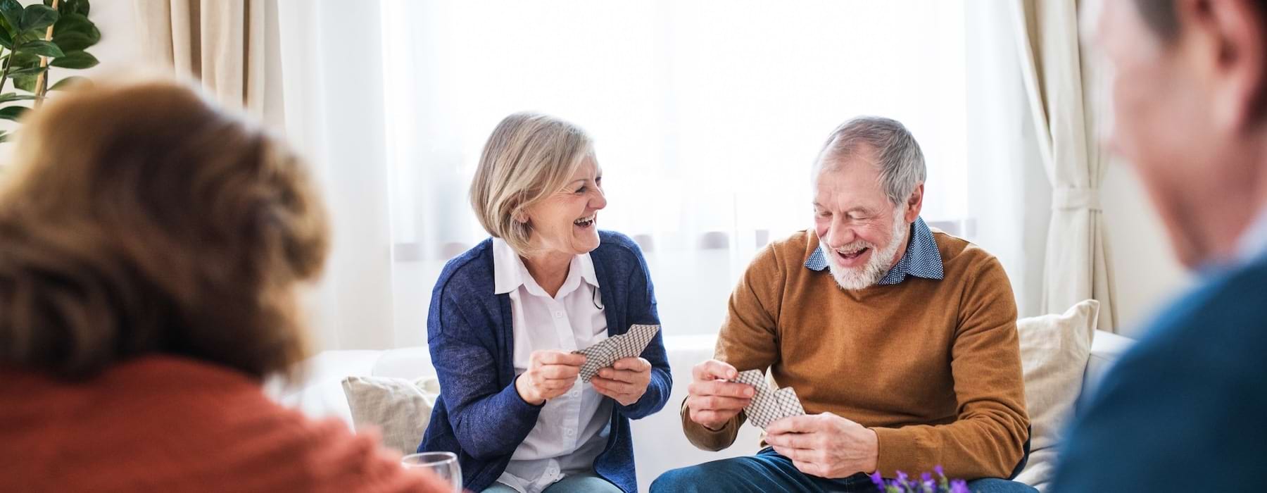 Residents playing cards and laughing at Outlook Gwinnett 55+ apartments in Buford, GA, featuring bright lighting.